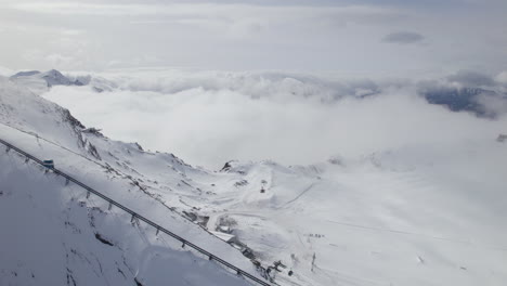 Aerial-view-of-gondola-driving-downhill-snowy-mountains-of-Austria---Dense-Clouds-covering-valley