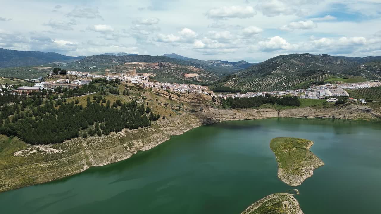 drone footage of Iznájar, a picturesque white village perched on a hilltop in Andalusia, Spain, with breathtaking views of the surrounding lake and rolling countryside.