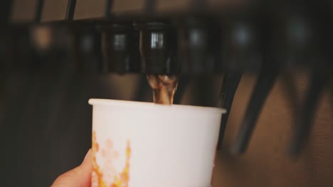 un hombre empujando la máquina con la mano de la cual la bebida dulce fluye hacia el vaso de papel
