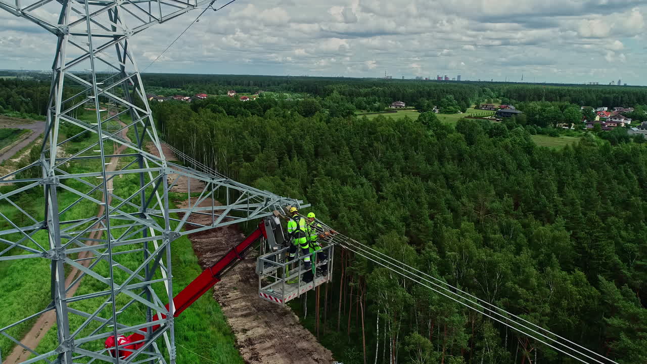 Nahaufnahme von Elektrikern, die an einem bewölkten Tag Stromleitungen an Strommasten in ländlicher Umgebung installieren.