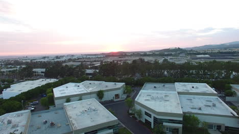 AERIAL:-Golden-hour-skyscapes-zooming-out-of-industrial-building-over-suburban-towns-and-businesses-in-Southern-California