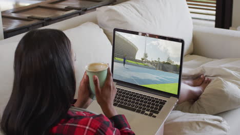 compuesto de una mujer sentada en casa sosteniendo un café viendo un evento de atletismo en una computadora portátil