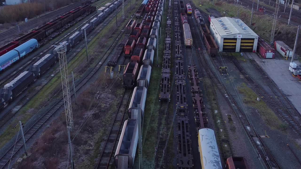 Sunrise aerial view of long railroad tracks with heavy diesel locomotive carriages and cargo container yard rising Birdseye