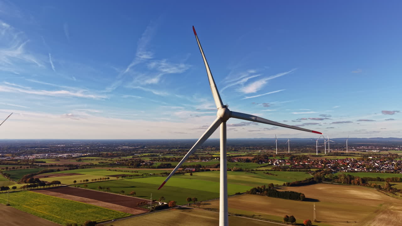 Majestic wind turbines rotating gracefully above lush green fields under a clear blue sky near a vibrant rural landscape