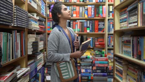 Asian-girl-standing-between-the-rows-of-bookshelves-searching-for-other-books,-Side-angle-shot