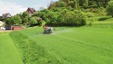 a farmer’s tractor being driven through a green field spraying, aerial