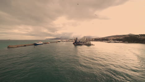 Cruise-ship-leaving-the-italian-harbour-of-Savona-at-dusk,-with-seagulls-flying-over-the-sea