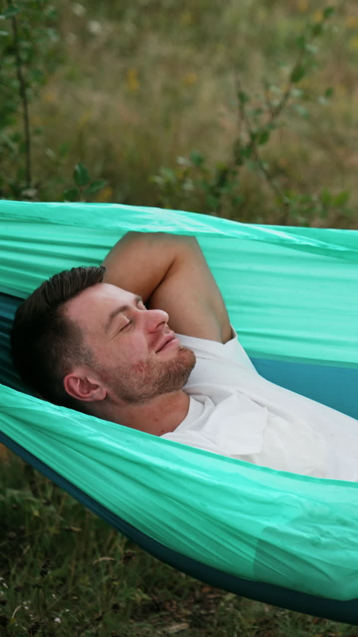 Relaxed Caucasian man swaying in hammock falling asleep. Person having rest in nature. Vertical video