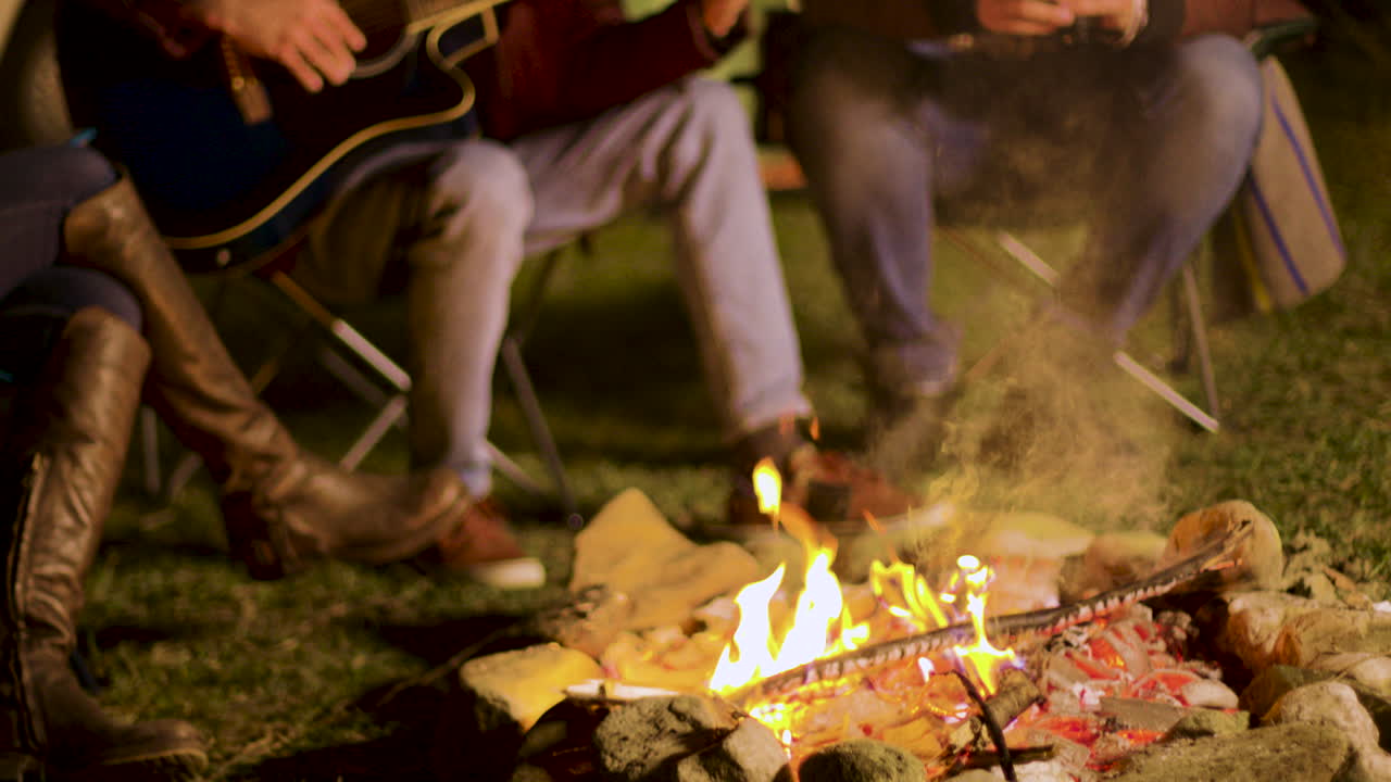Camping fire burning while man's singing on guitar