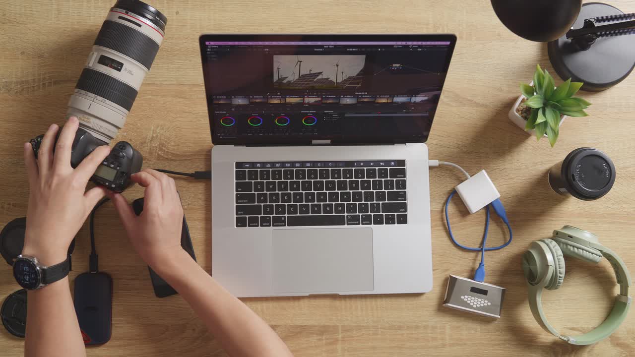 vista superior de cerca de las manos del calificador de color masculino poniendo la tarjeta de memoria en una computadora portátil y luego eligiendo el video en el espacio de trabajo en casa