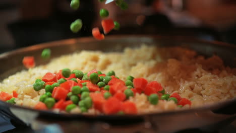 adding peas and diced carrots to the savory rice dish - isolated slow motion