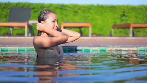 portrait of passionate young asian woman touches her wet hair in the swimming pool of the exotic hotel and turning her sight towards the camera