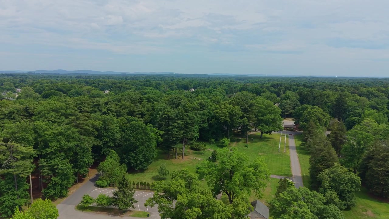 Ripresa aerea con drone di un'area di parcheggio circondata da una fitta foresta verde e paesaggio suburbano, Springfield, Massachusetts, USA