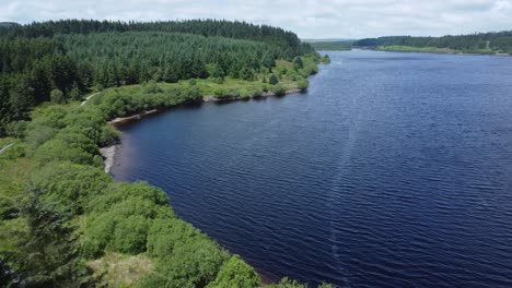 idyllic blue water reservoir lake woodland hiking walk aerial view fast reverse above forest trees