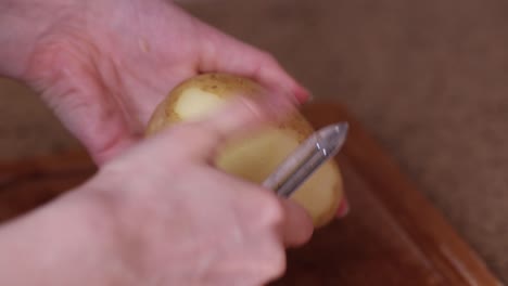 cerrar manos de mujer pelando patatas con pelador de verduras encima de la mesa de la cocina