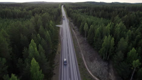 Stunning-Drone-Shot-of-Lonely-Forest-Road-in-Northern-Finland,-Car-Passing-By,-Truck-Carrying-Wood