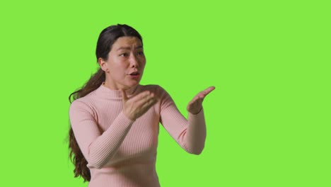 초록색 스크린 앞 에 서 있는 좌절 된 분노 한 여자 의 스튜디오 초상화 가 카메라 1 을 벗어난 사람 에게 소리 지르고 있다