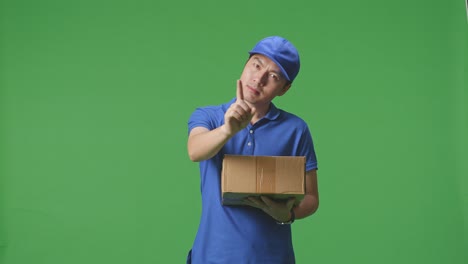 mensajero masculino asiático en uniforme azul que no muestra ningún gesto mientras entrega una caja de cartón en el fondo de la pantalla verde en el estudio