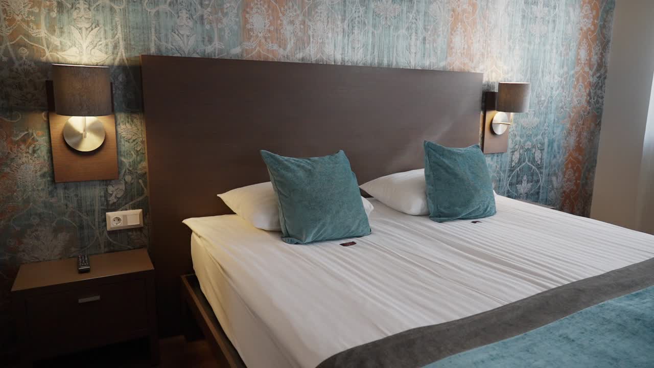 Modern hotel bedroom with double bed, teal pillows, and artistic wallpaper