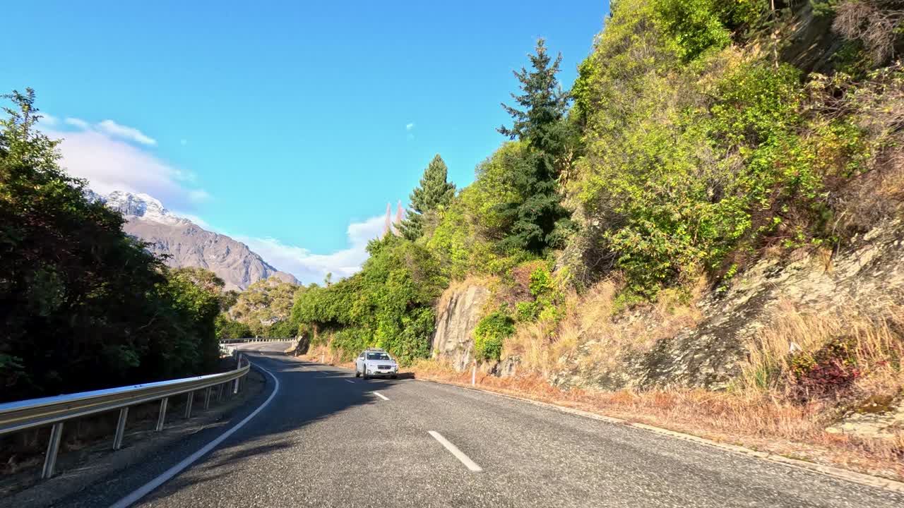 Car travels winding mountain road with lush greenery, clear daylight, and steady forward camera movement