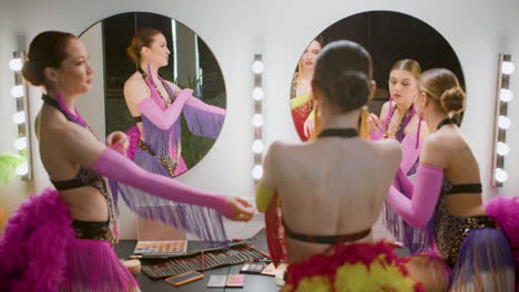 female dancer using make up while her colleagues are getting ready for the show