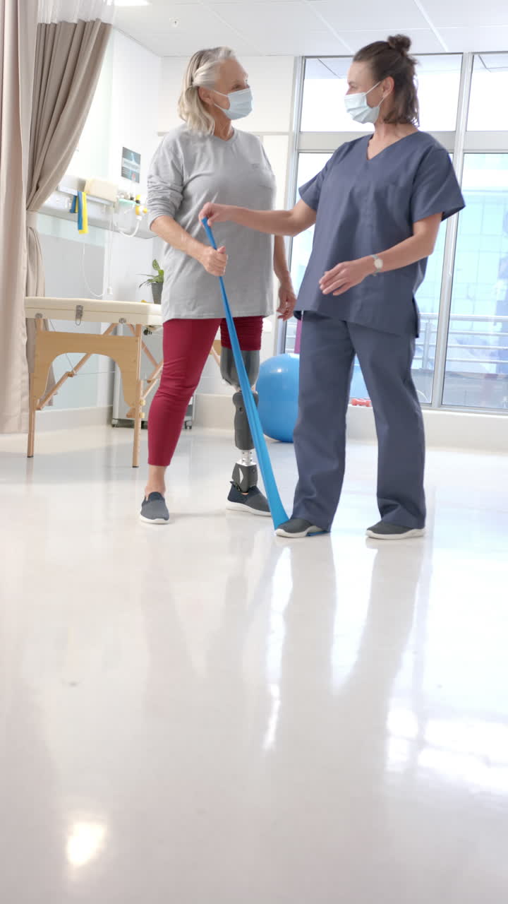 Vertical video of caucasian female physiotherapist helping female patient to exercise with bands