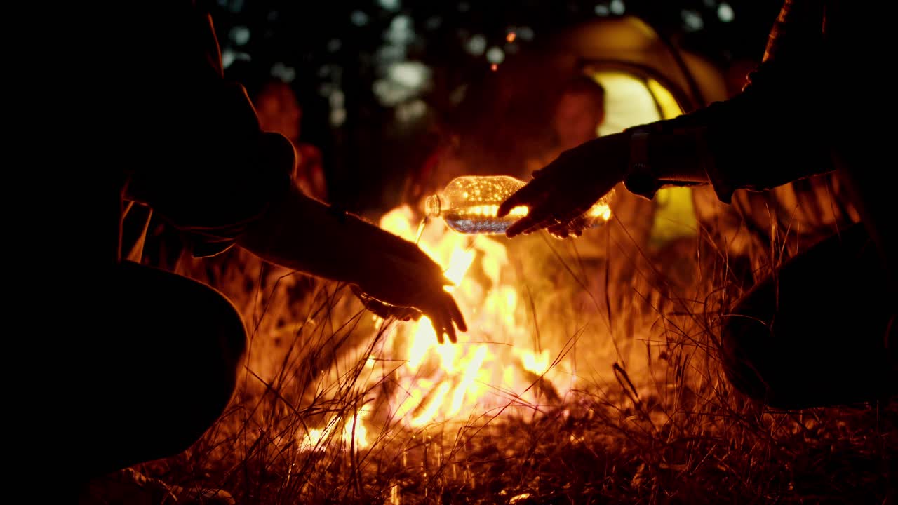 한 사람이 밤의 숲에서 화재의 배경에 플라스틱 투명한 병에서 한 남자의 손에 물을 부어.