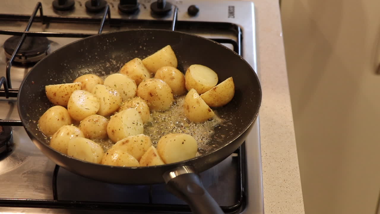 Small potatoes being sautéed in a pan with bubbling butter and garlic on a gas stove