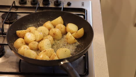 small potatoes being sautéed in a pan with bubbling butter and garlic on a gas stove