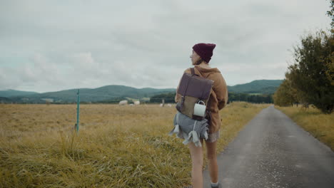 Woman-with-backpack-walking-by-field-under-sky