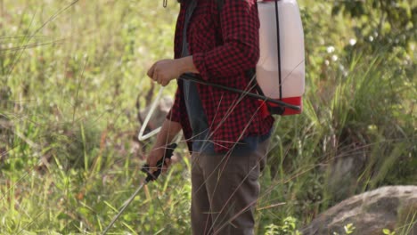 medium shot of a man working with a backpack sprayer in the forest, he wears a red shirt and a hat