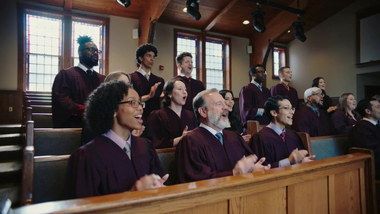 Singing choir members following hymn cue, clapping and leaning in pews wearing maroon robes