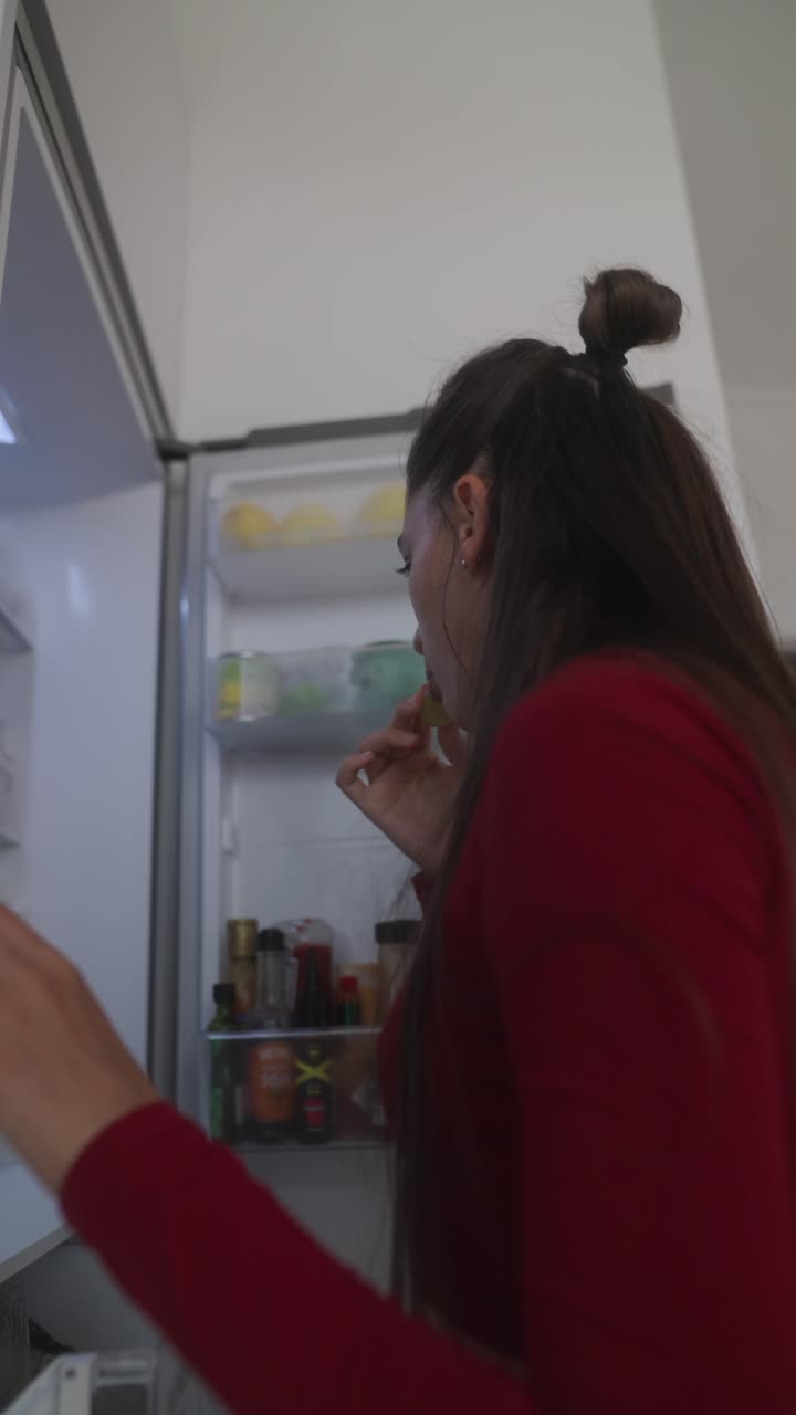 Woman eating fruit from refrigerator
