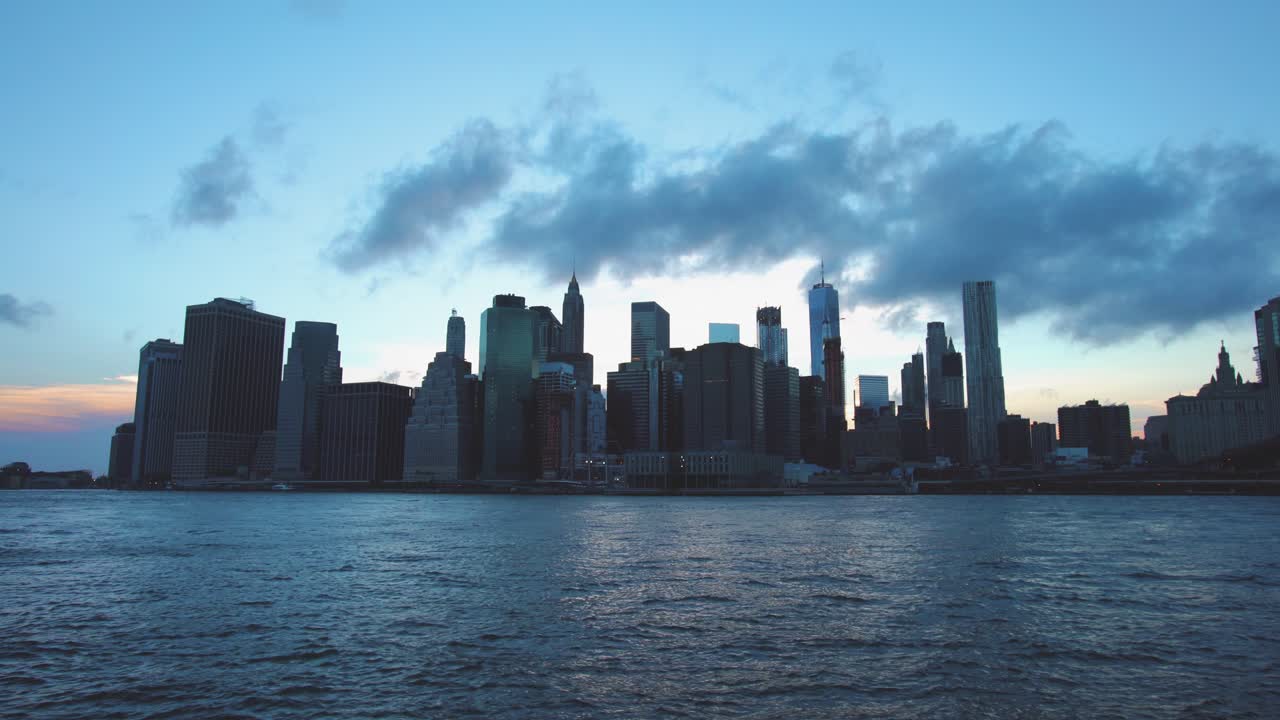 NYC: Downtown Manhattan skyline from Dumbo Brooklyn, just after sunset  with fast moving clouds shrouding the spire of One World Trade, and the East River in the foreground - New York City, USA