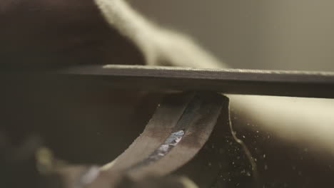 sawdust flies as a man uses a file to sand and smooth a wooden knife handle