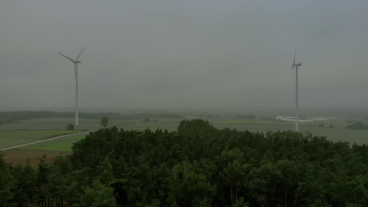 높은 나무 근처의 풍차 근처의 항공 영상, 지평선의 안개가 자욱한 기상 조건, 드론 촬영 비디오 4k
