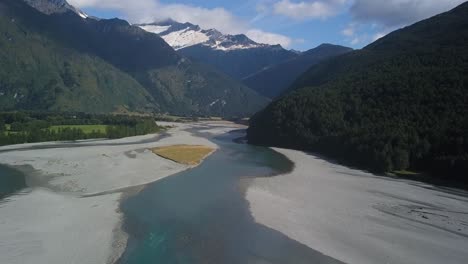 Ascending-shot-of-an-icy-river-thawing-out-on-a-sunny-day,-with-an-ice-covered-glacier-in-the-distance