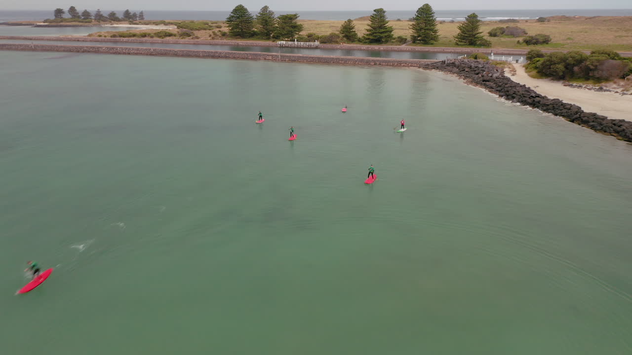 Aerial flyover group of SUP Paddler on clear water of Port Fairy in Australia.