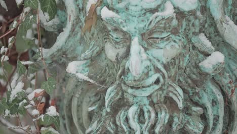 Sculpture of a faun covered with patina and adorned with a creeping ivy in the snowfall. A slow-motion parallax shot.