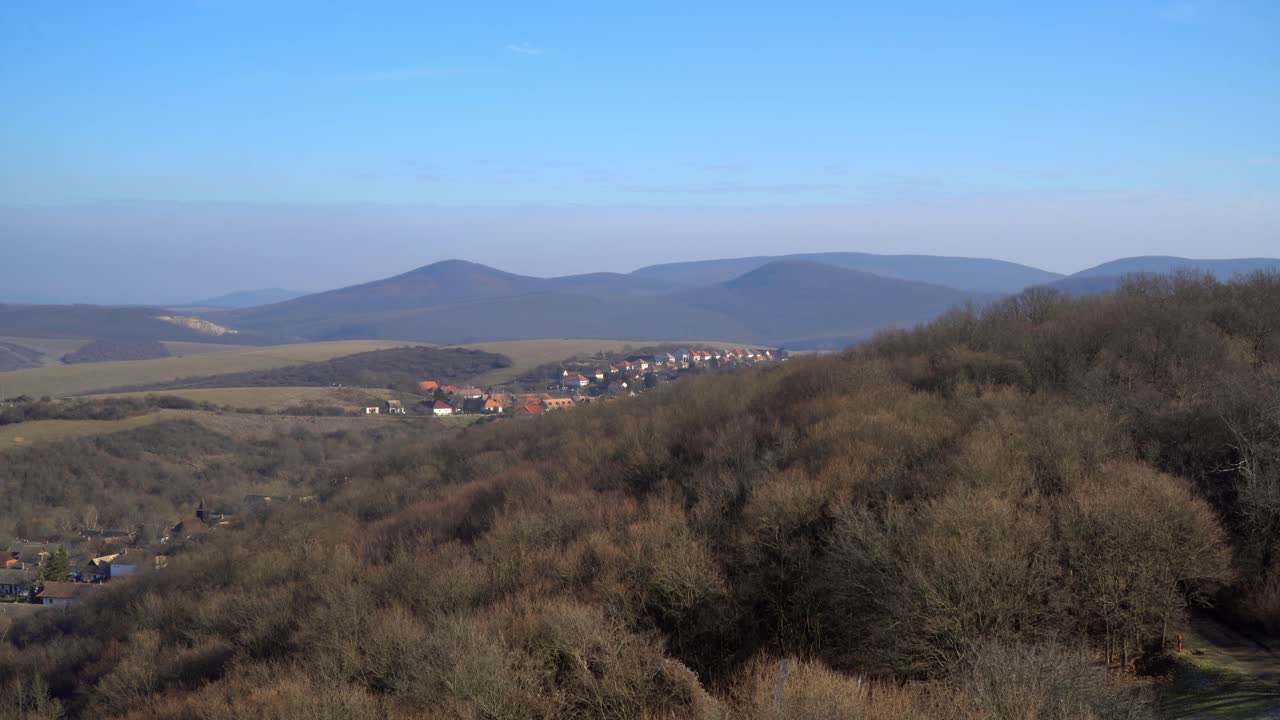 Aerial view of Hollókő, Hungary, showcasing rolling hills, valleys, and a traditional village. The UNESCO-listed site blends nature and heritage, offering a glimpse into rural European charm.