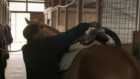 man placing a saddle on a brown horse