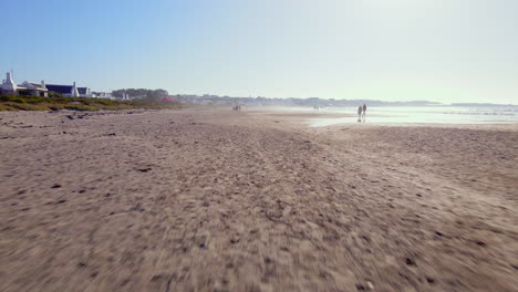 Low-aerial-dolly-riser-over-Paternoster-beach-with-strolling-tourists,-Weskus