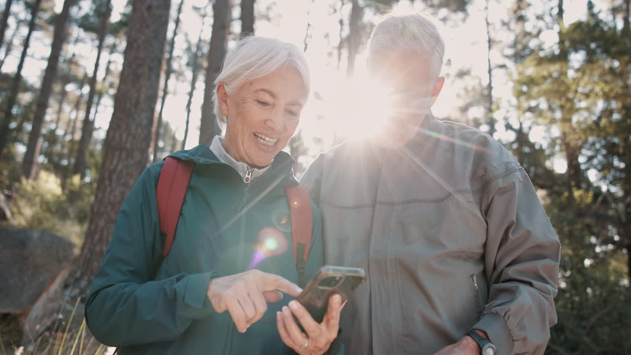 una pareja de ancianos haciendo senderismo y usando un teléfono inteligente en el bosque.
