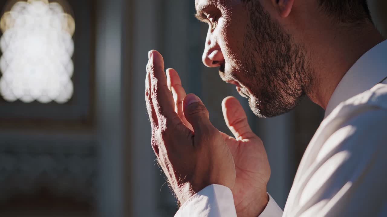 The video captures a serene moment of prayer, focusing on a man's hands in a place of worship
