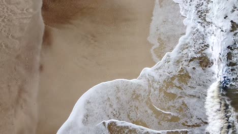 Aerial-view-of-waves-becoming-foam-in-the-coastline-with-only-the-sand-as-witness
