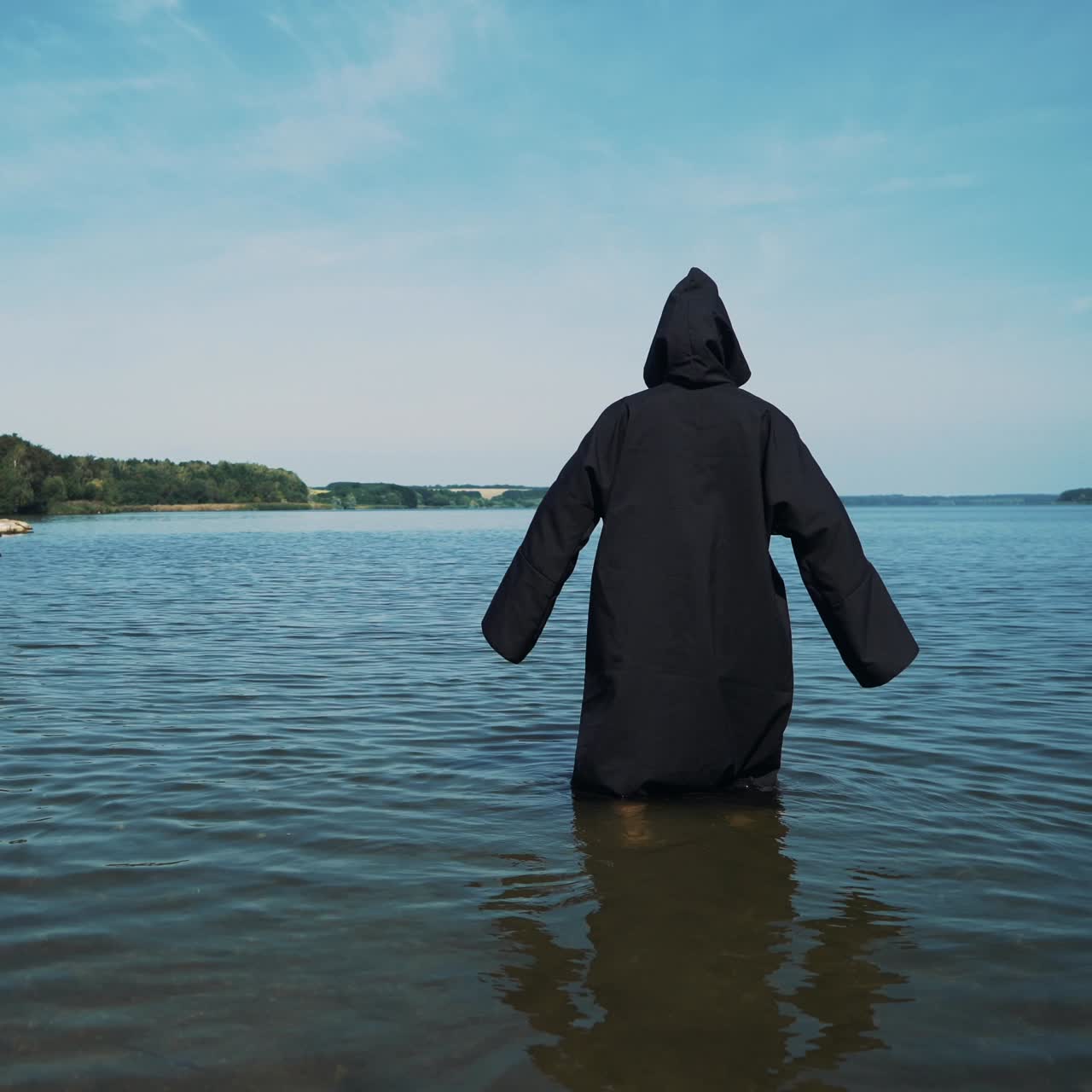 Terrible witch in black mantle in the water outdoor.