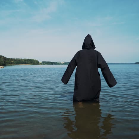 terrible witch in black mantle in the water outdoor.