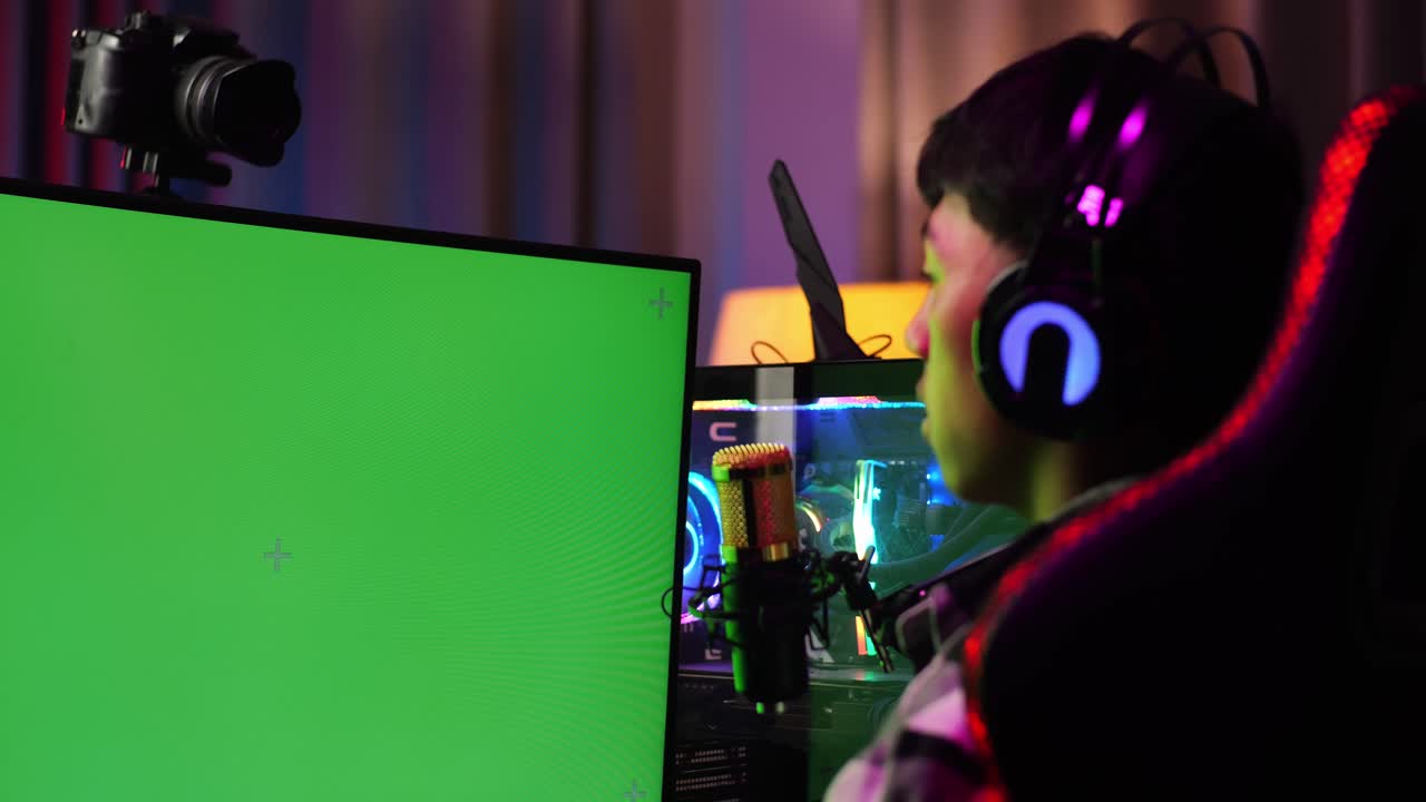 Close Up Back View Of Asian Boy Streamer Using Green Screen Personal Computer. Yawning And Sleeping, Desk Illuminated By Rgb Led Strip Light