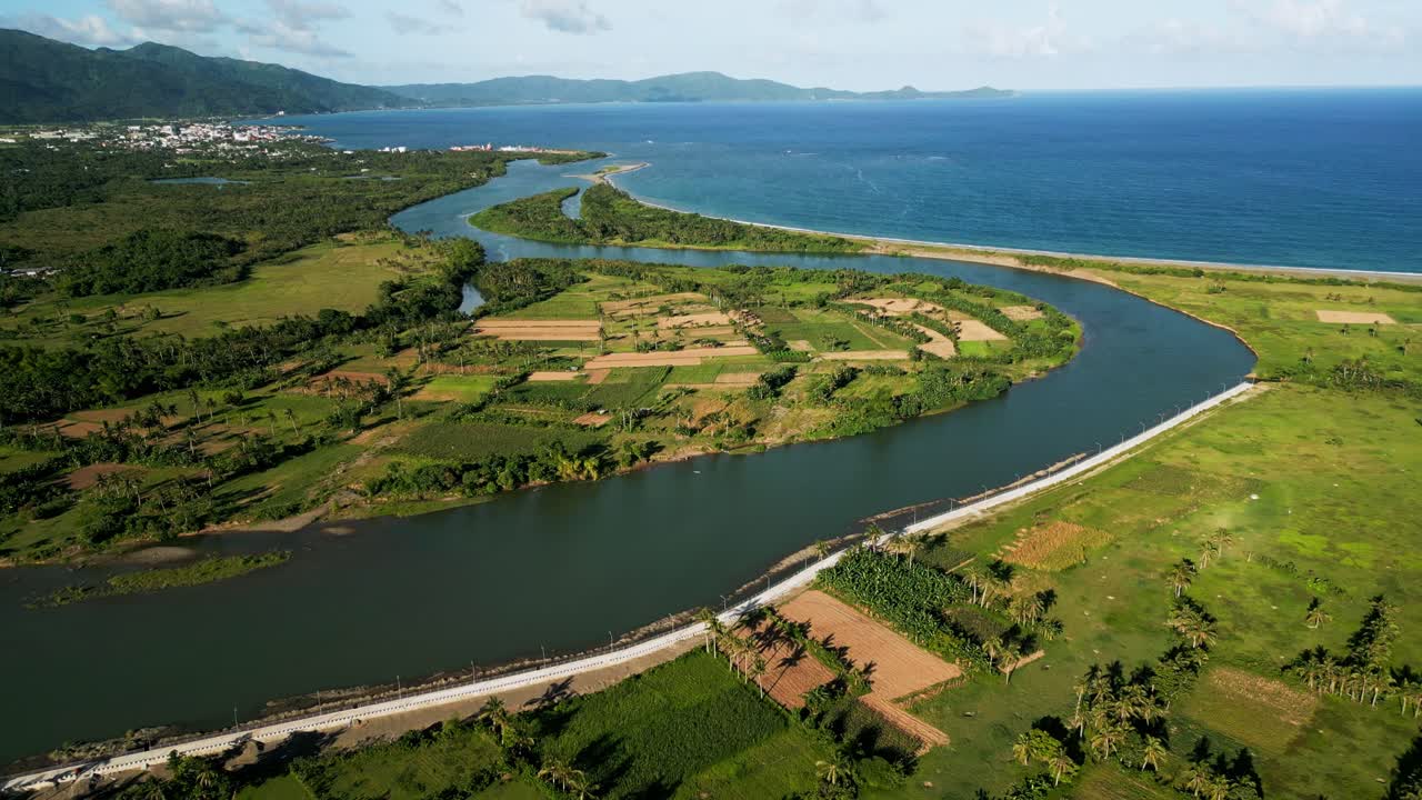 Aerial flyover shot of serpentine river and river mouth surrounded by lush fields and tropical island coastline - Catanduanes, Philippines