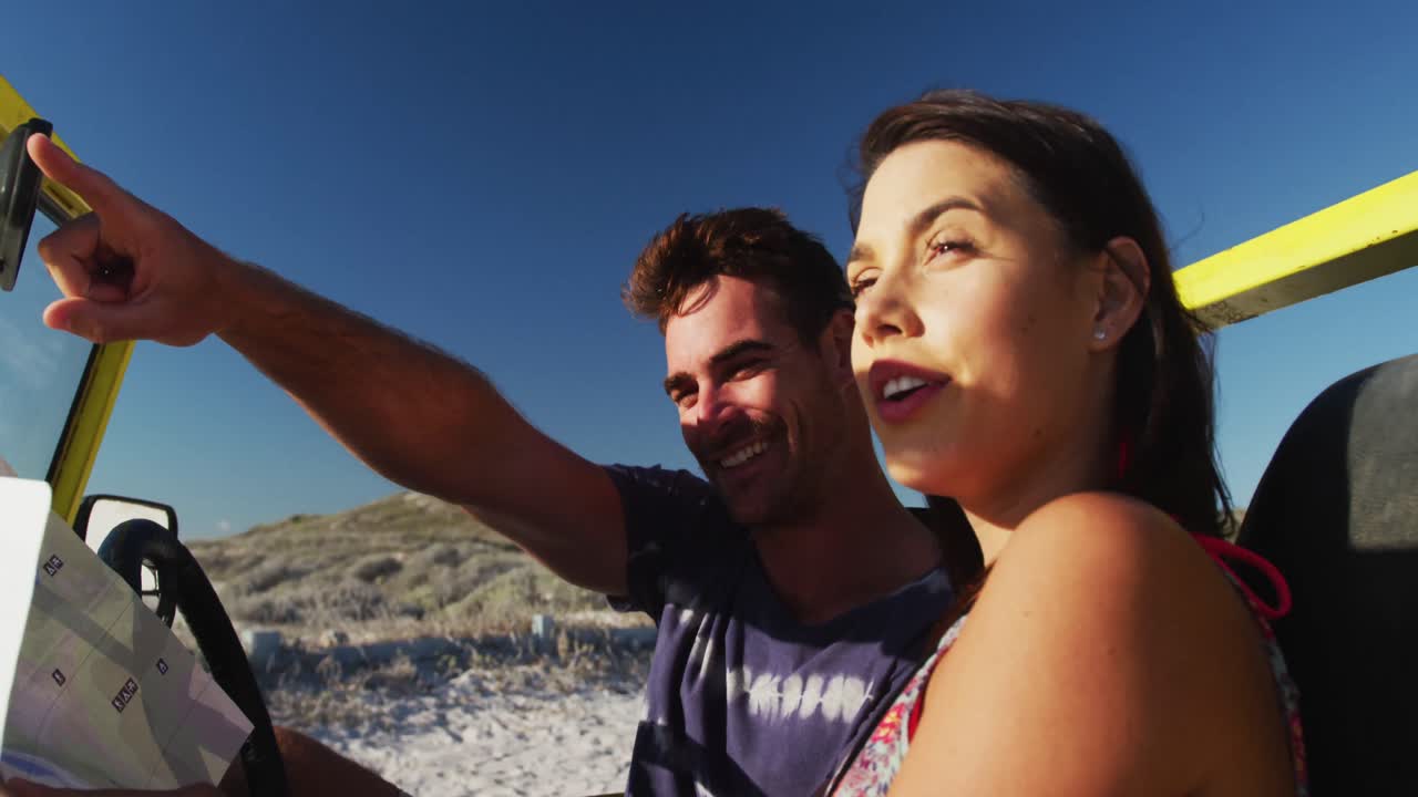 pareja caucásica de pie cerca de la playa buggy por el mar leyendo un mapa